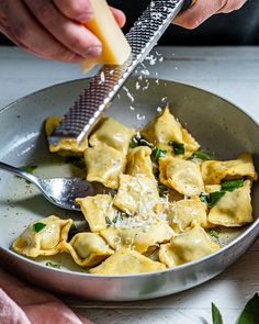 someone grating cheese on top of ravioli in a pan