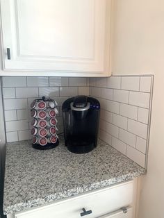 two soda cans sitting on top of a counter next to a black coffee maker and white cabinets