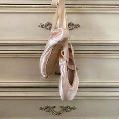 two ballet shoes hanging on a wall next to an old dresser with drawers in the background