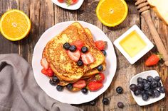 french toast with strawberries, blueberries and oranges on a plate next to butter