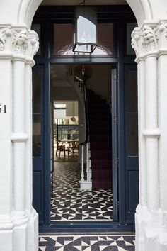 the entrance to an elegant home with black and white tile flooring, columns and chandelier