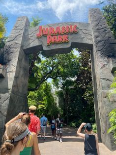 people are walking under the entrance to an amusement park that looks like a jungle park