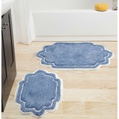 two bathroom rugs on the floor in front of a bathtub