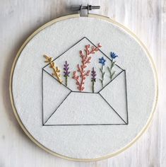 an envelope with flowers in it is embroidered on a piece of white fabric and hangs from a hoop