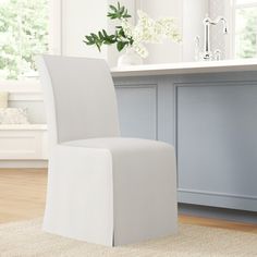 a white chair sitting on top of a wooden floor next to a vase filled with flowers