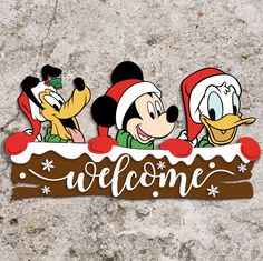 mickey mouse and donald duck welcome sign with santa hats on it's head, standing in front of a stone wall