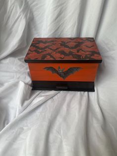 an orange and black box with bats painted on the lid sitting on a white sheet