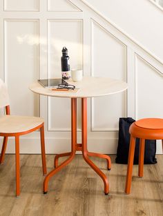 an orange table and two chairs in front of a white wall with wood flooring