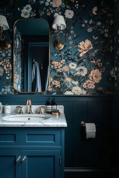 a blue bathroom with floral wallpaper and gold faucet, sink, mirror