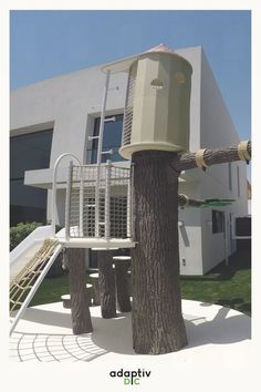 a tree that is next to a building with a slide in front of it and a house behind it