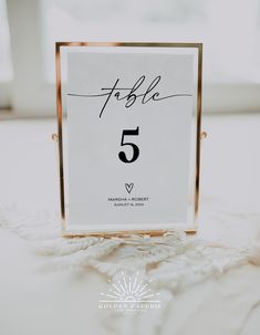 a table number is placed on top of a white doily with a gold frame