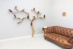 a brown leather couch sitting in front of a tree shaped book shelf on the wall