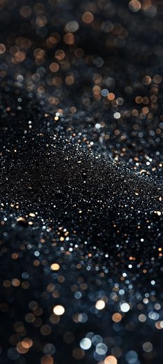 an image of some black and gold sparkles on the surface with blurry lights in the background