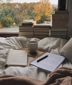 an open book, coffee cup and pen on top of a bed in front of a window