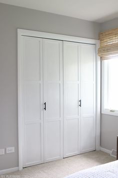 a bedroom with white closet doors and carpeted flooring in front of a window