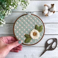 someone is working on an embroidery project with scissors and flowers in front of the hoop