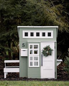 a small green and white shed with wreath on the door, window sill, and bench