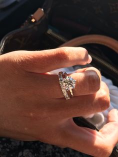 a woman's hand with a diamond ring on top of her finger and purse in the background