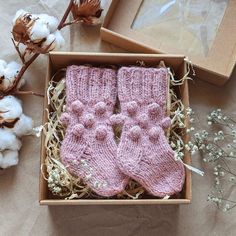 two pink knitted mittens in a box next to cotton flowers