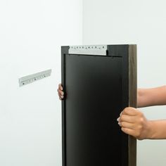 a person is holding onto a black cabinet with a measuring tape on it and another hand reaching for the door