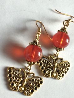 Rustic Butterfly Charm Earrings they are made with a beautiful detailed Butterfly Charm and Antique Spacers they are also having a Rust Tone Jade Style Translucent Bead they are 1.5” long Amber Beaded Drop Earrings For Gift, Handmade Amber Round Bead Earrings, Handmade Amber Beaded Round Earrings, Handmade Amber Earrings With Round Beads, Amber Beaded Earrings For Gift, Handmade Red Czech Glass Beaded Earrings, Amber Beaded Dangle Earrings, Nickel-free Red Beaded Round Earrings, Red Dangle Earrings With Ear Wire