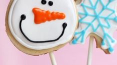 two decorated cookies on sticks with icing and snowman faces in the middle one is frosted, the other has an orange bow tie