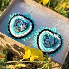 two blue and white beaded earrings sitting on top of a box next to flowers