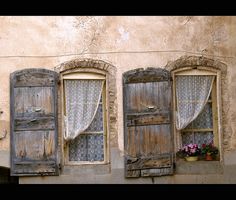 three old windows with curtains and flower pots