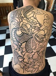 the back of a man's body covered in black and white ink with dragon tattoos on