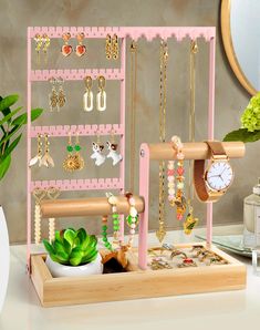 a pink jewelry rack with various necklaces and rings on it next to a potted plant