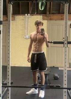 a shirtless man takes a selfie in the mirror while standing on a gym floor