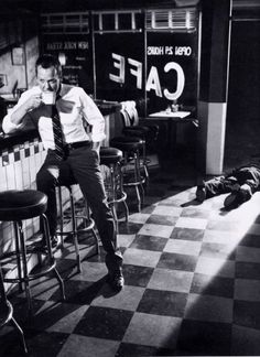 black and white photograph of a man sitting at a bar with his feet on the counter