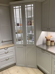 a kitchen with white cabinets and wooden flooring next to an open pantry door that has glass doors on both sides