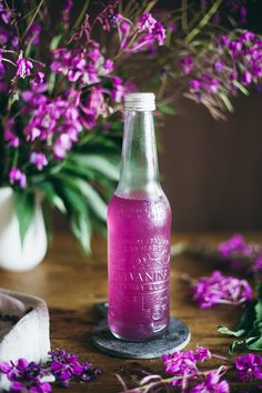 a glass bottle filled with pink liquid next to purple flowers