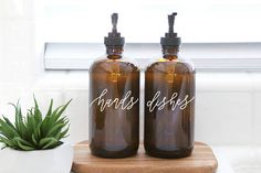 two brown glass bottles sitting on top of a wooden table next to a potted plant