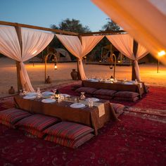 an outdoor dining area with white drapes and red rugs, lit by candles