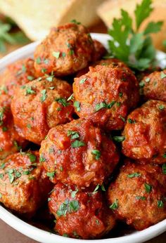 a white bowl filled with meatballs covered in marinara sauce and garnished with parsley