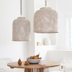 two lamps hanging from the ceiling above a wooden table with white chairs and bowls of fruit on it