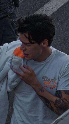 a man with tattoos on his arm drinking from a cup while standing in the street