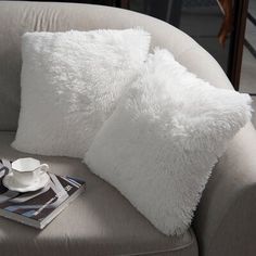 two white pillows sitting on top of a couch next to a cup and saucer