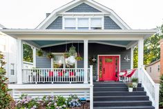 a red door sits on the front porch of a gray house with white railings