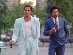 two men in suits are walking down the street with one man wearing a blue suit