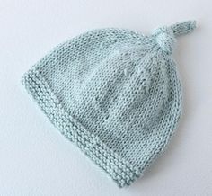 a blue knitted hat with a knot on the brim is laying against a white wall