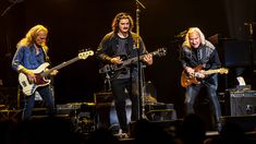 three men are playing guitars on stage