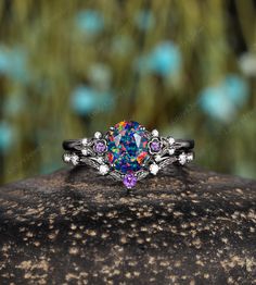 a ring with an opal colored stone surrounded by white and pink stones on top of a rock