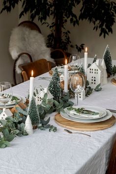 the table is set with candles, plates and greenery