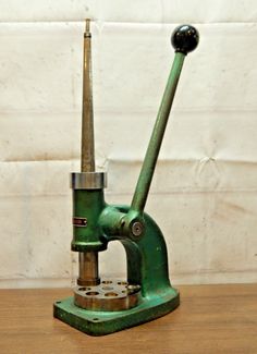 an old green microscope on a wooden table with a white wall in the back ground