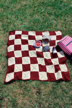 a red and white blanket sitting on top of a grass covered field next to a bag