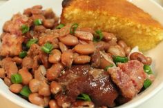 a white bowl filled with beans next to a piece of cornbread on top of a table