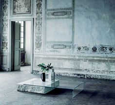 an empty room with a table, chair and vase on the floor in front of it